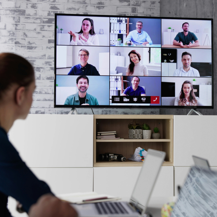 Person attending a large video conference displayed on a wall screen, illustrating professional webinar hosting and multi-participant interaction.